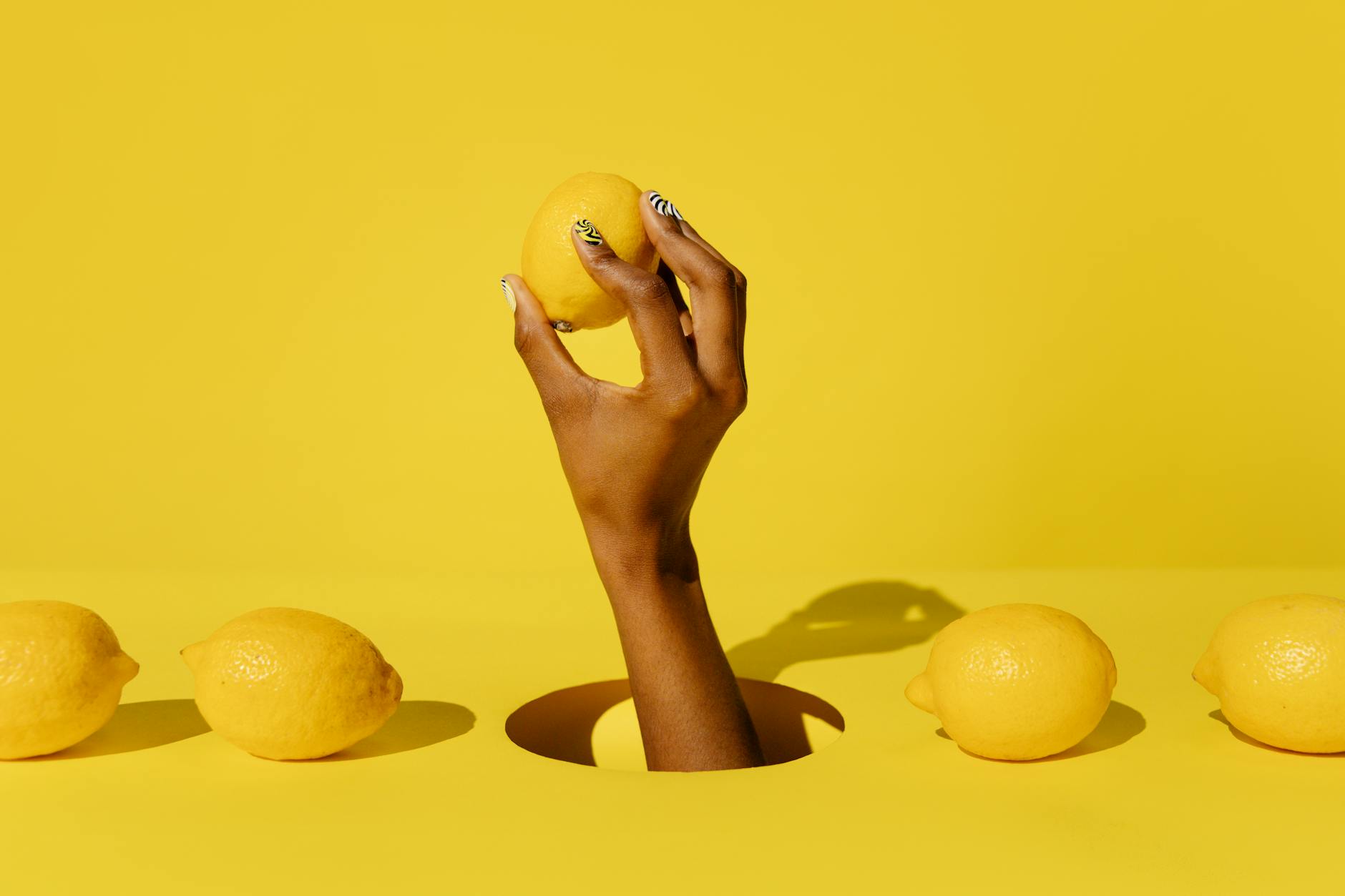 A hand holding a lemon against a bright yellow background, symbolizing the lemon vibrator and fresh sexual wellness