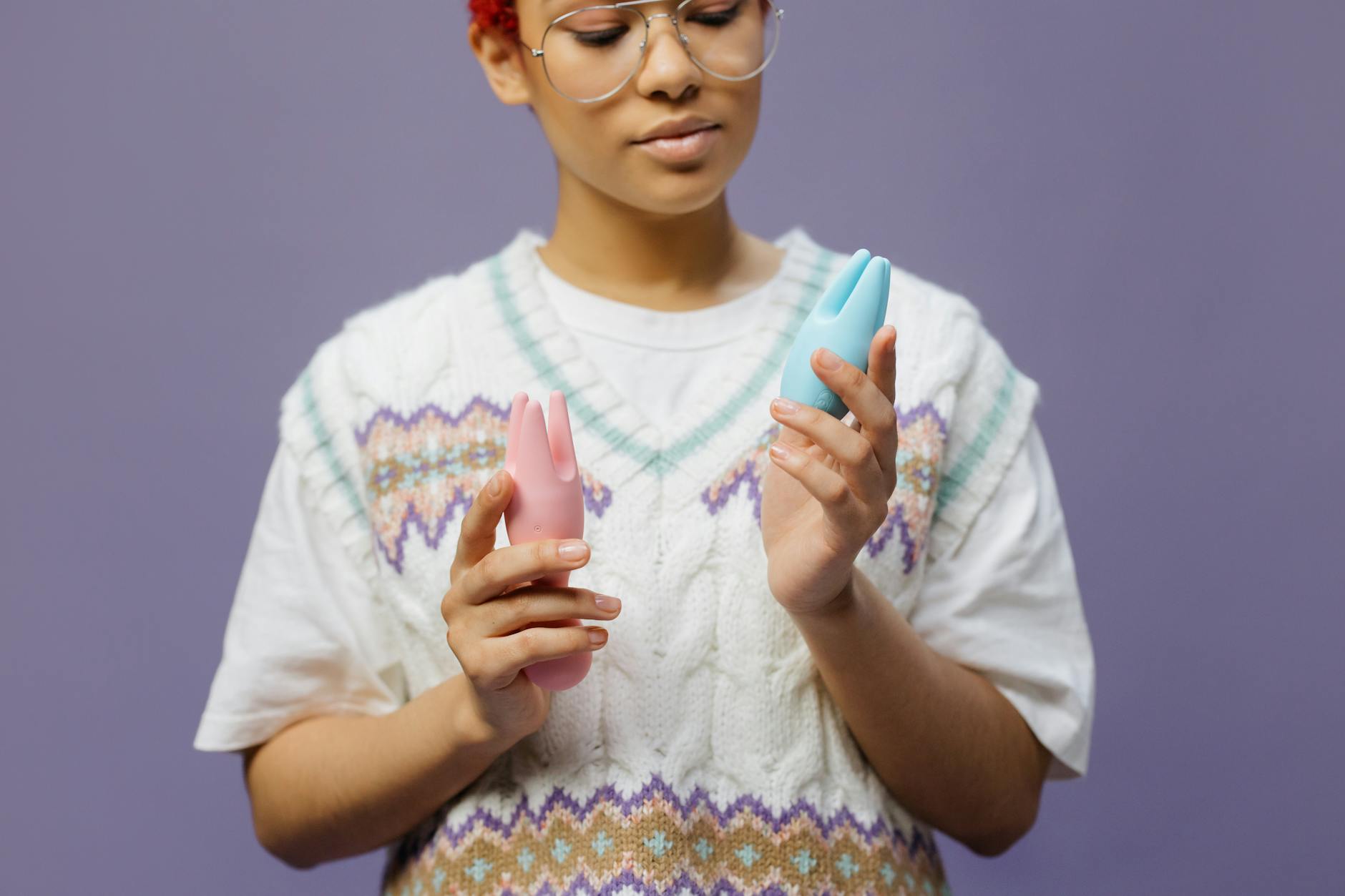 Woman with eyeglasses thoughtfully holding blue and pink silicone vibrators