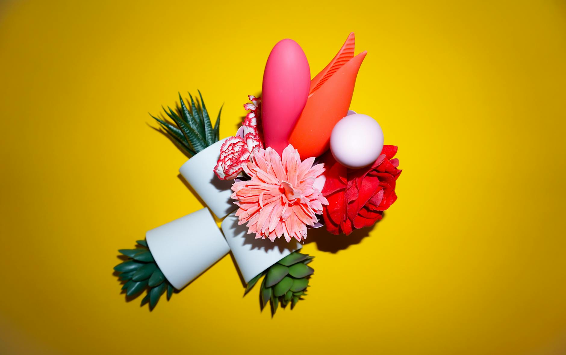 Two hands holding pink and blue silicone vibrators against a pastel background.