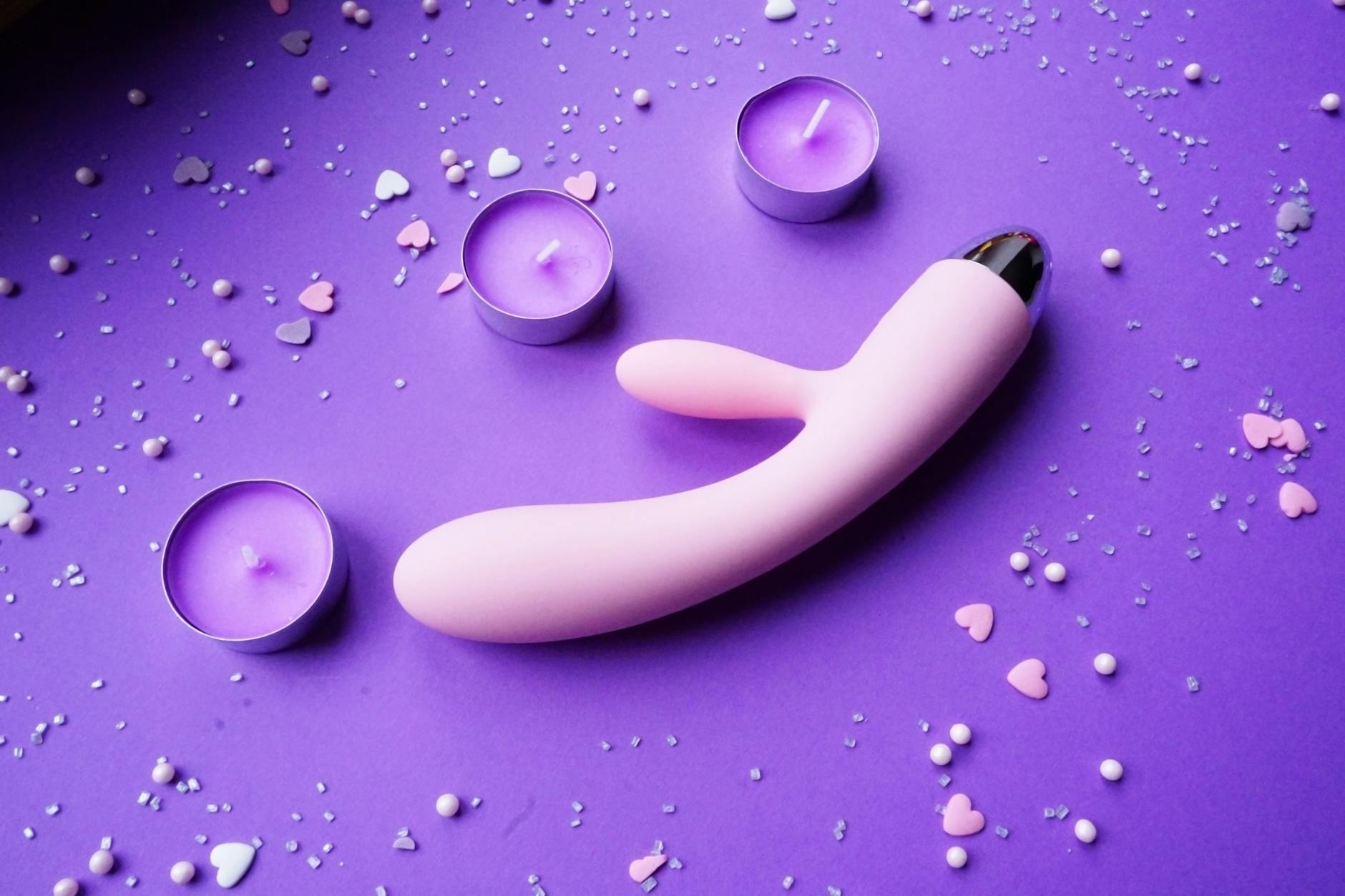 Pink lemon clitoral vibrator on purple background with heart confetti and candles for couples intimacy